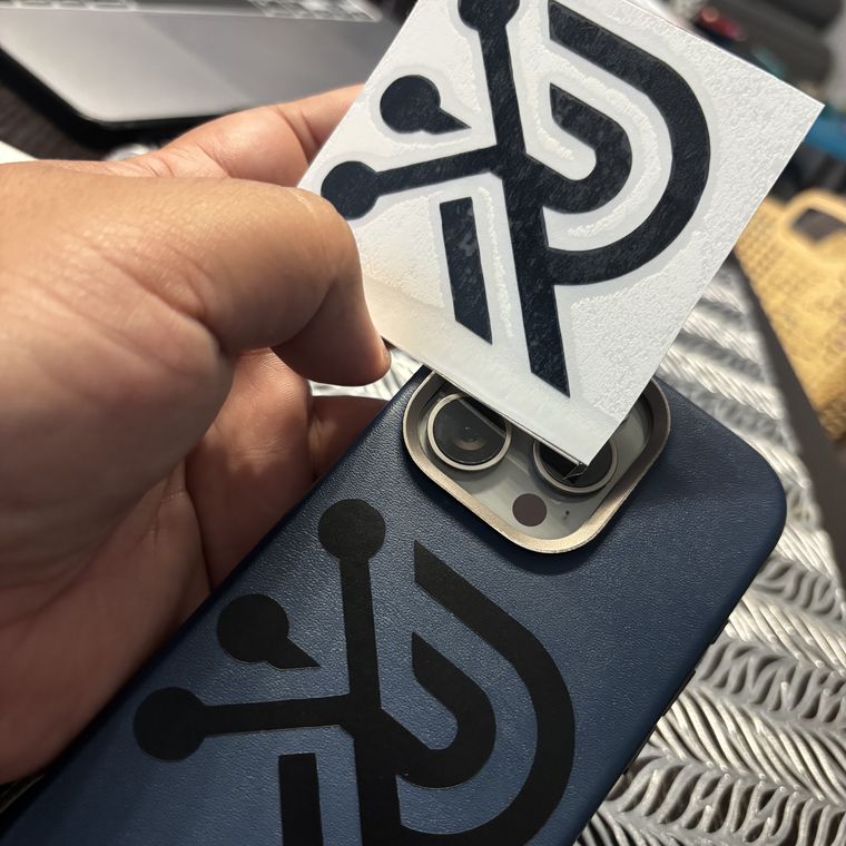 El logo recién cortado en vinil, sostenido junto a la funda de un teléfono donde ya está puesto